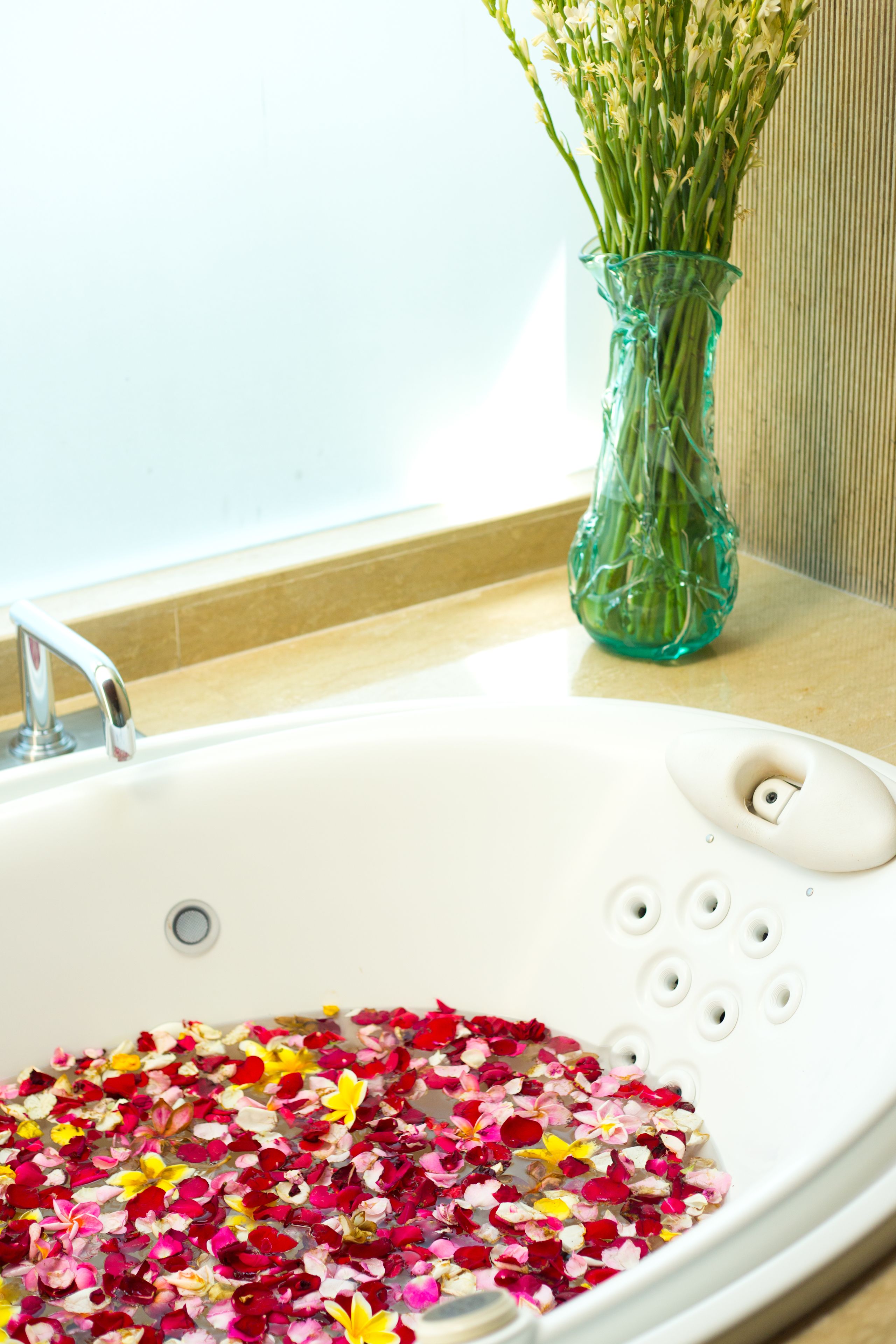 A bathtub filled with water and flower petals, a glass vase with flowers, and a bathroom sink.