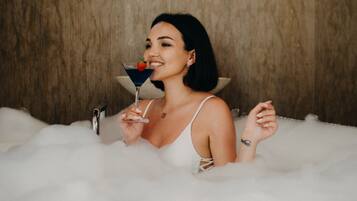 A person in a bathtub filled with bubbles, holding a drink with a garnish.