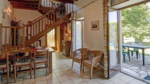 A spacious interior with a wooden staircase, a dining area with chairs, and a view through a glass door to an outdoor patio. - Cottage 80m² with Terrace, Wifi and Pets Allowed (Notre-Dame-de-Boisset)