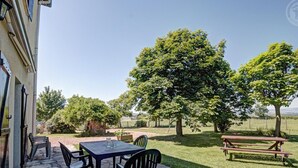 A patio with a table and chairs, a stone floor, and a view of a grassy area with trees. - Cottage 80m² with Terrace, Wifi and Pets Allowed (Notre-Dame-de-Boisset)