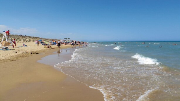 Una playa con gente tomando el sol y nadando.