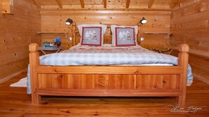 Quarto de cabana de madeira com uma cama, duas mesinhas de cabeceira e teto de madeira.