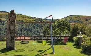 Un espace extérieur verdoyant avec une balançoire, une chaise rouge et une structure en pierre.