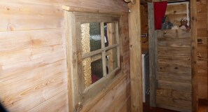 Une pièce en bois avec une fenêtre, une porte et une petite étagère ornée d’objets décoratifs.