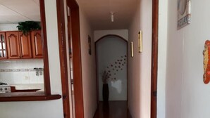 A hallway with a wooden door leading to a room, a tiled floor, and a kitchen area with cabinets and a stove. - Posada Nativa Nilvis Place (San Andrés)