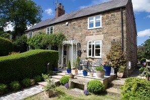 A stone house with a porch, potted plants, and a small table with chairs.