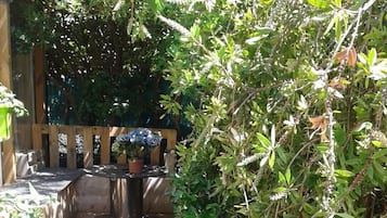 Eine Holzterrasse mit Sitzgelegenheit, umgeben von üppigem Grün und Kübelpflanzen.