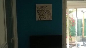 A room with a blue wall, a mounted tiger artwork, a TV on a white stand, and a sliding glass door leading outside.
