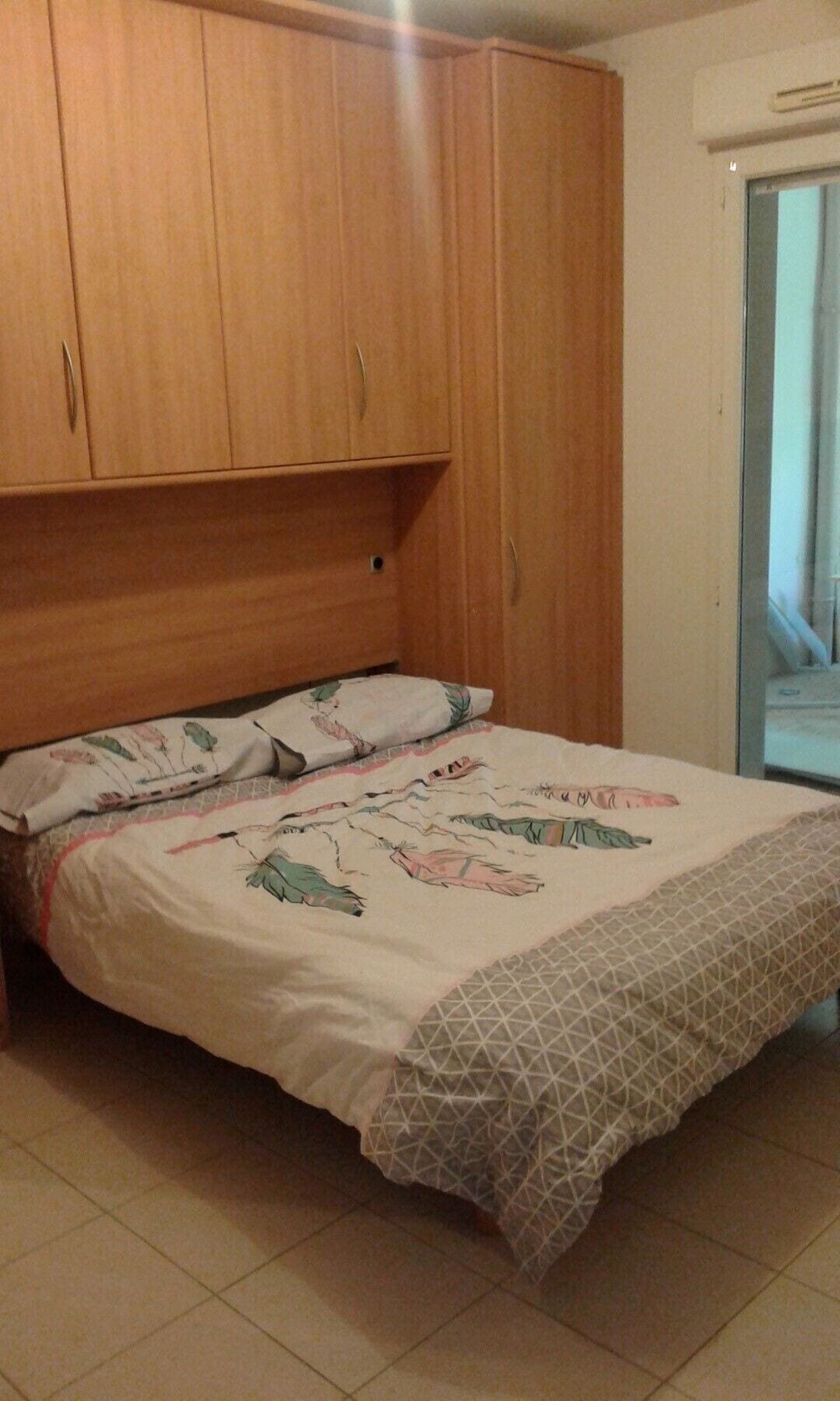 Ein Schlafzimmer mit einem Bett, einem Holzschrank und einem Fenster mit Klimaanlage.