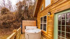 Une cabane en bois avec un jacuzzi sur la terrasse, une fenêtre éclairée et une porte.