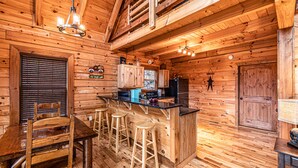 L’intérieur d’un chalet en bois comprend un coin bar, une table à manger en bois et des tabourets.