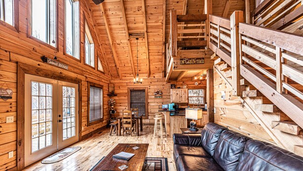 L’intérieur d’une cabane en rondins, avec un escalier en bois, un salon doté d’un canapé en cuir, un coin repas et une cuisine.