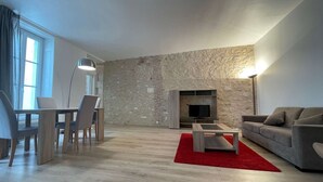 A modern living room with a stone wall, a flat-screen TV, a sofa, a coffee table, and a dining area with chairs and a table.