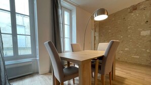 A dining area with a wooden table and four chairs, a floor lamp, and a view through large windows.