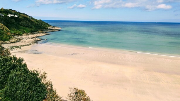 Una playa con aguas cristalinas, una orilla arenosa y un promontorio cubierto de bosque.
