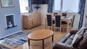 Una sala de estar con una mesa de madera, un sofá de cuero y un televisor montado en la pared.