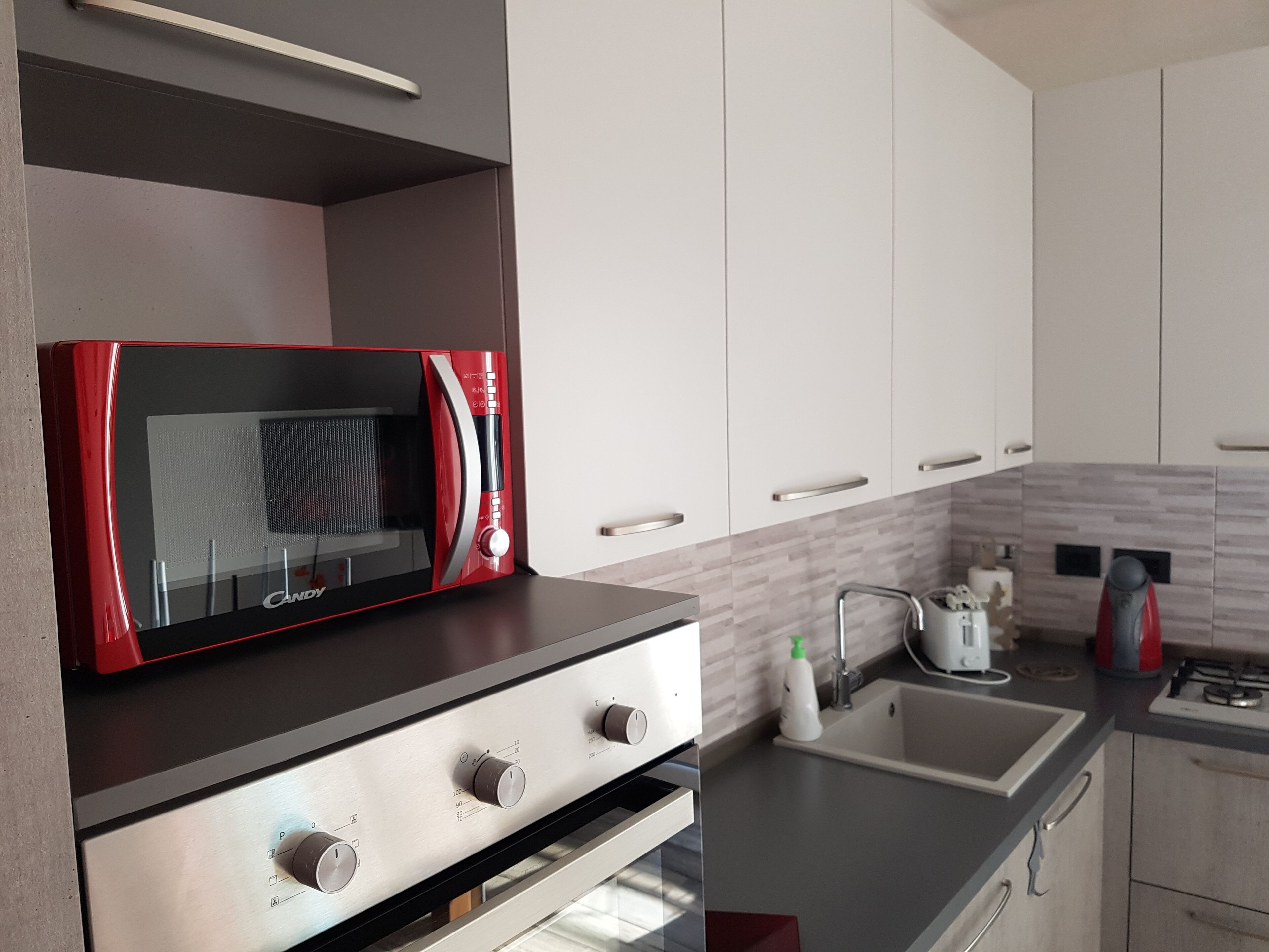 Una cocina con armarios blancos, un microondas rojo y electrodomésticos de acero inoxidable.