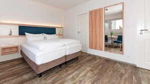 Une chambre d’hôtel moderne dotée d’un grand lit, d’un parquet en bois, d’une armoire intégrée et d’un miroir qui reflète un coin repas.