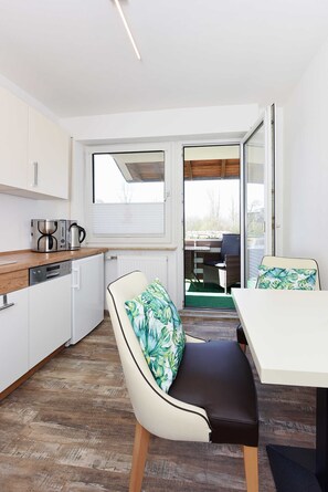 Cozinha compacta com eletrodomésticos modernos, área de refeições com mesa e cadeiras, e uma porta de vidro deslizante que dá acesso a um espaço de estar ao ar livre.
