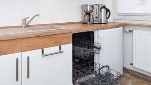 Une cuisine moderne avec des armoires blanches, un plan de travail en bois, un lave-vaisselle encastré et une machine à café.