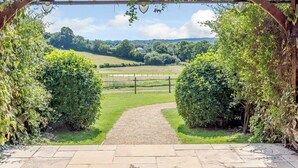 A wooden pergola with hanging lamps and a gravel path leading to a fenced field. - Castlemans Stables East (Sedlescombe, near Battle)