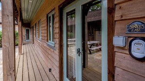 A wooden cabin with a covered porch, a door with a glass panel, and a sign reading "Stables East". - Castlemans Stables East (Sedlescombe, near Battle)