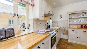 A kitchen with a wooden countertop, white cabinets, a stove, and a window with striped valance. - Castlemans Stables East (Sedlescombe, near Battle)