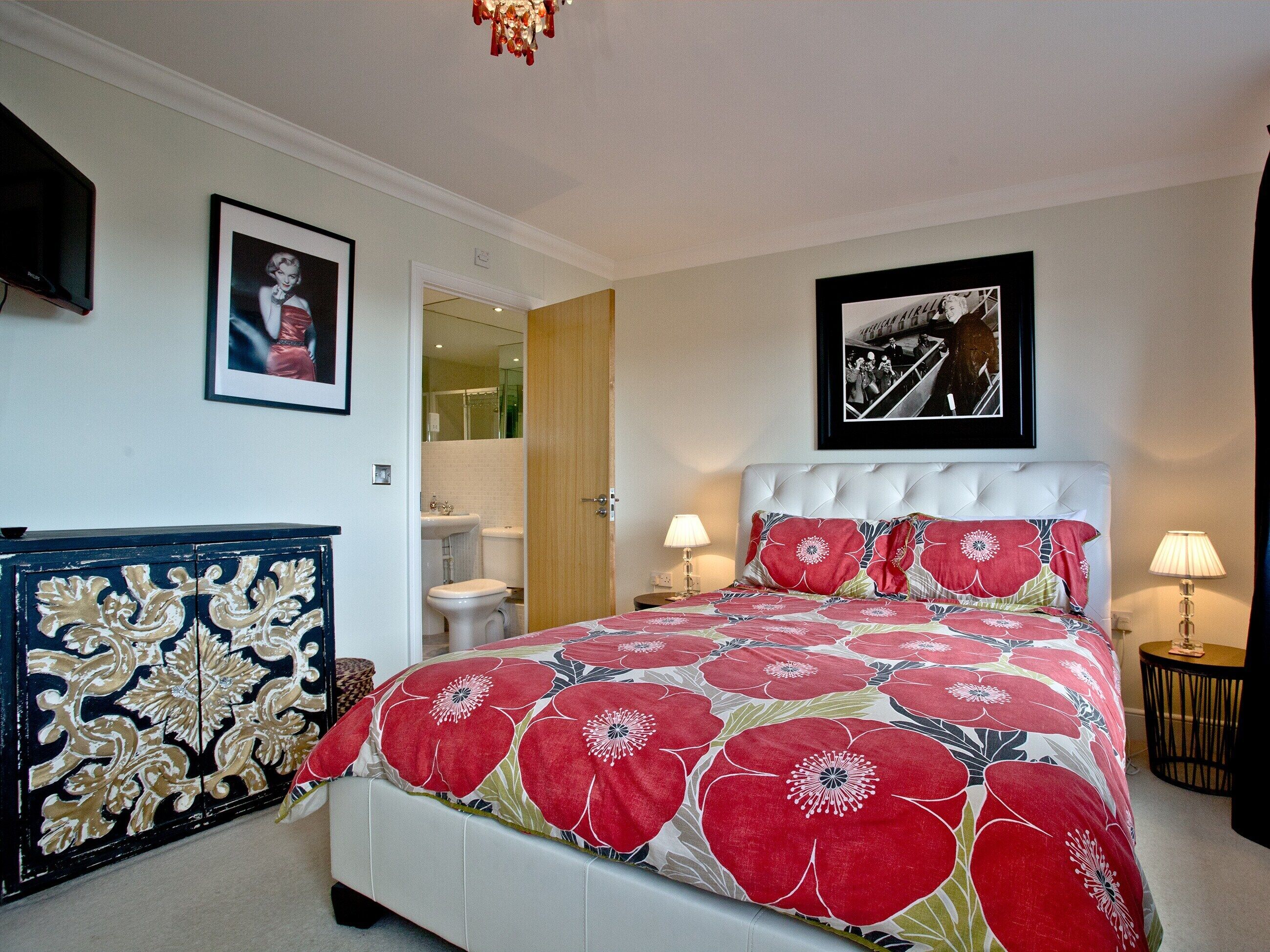 Une chambre à coucher comprenant un lit, deux tables de chevet, une commode, un miroir et une porte donnant sur une salle de bain.