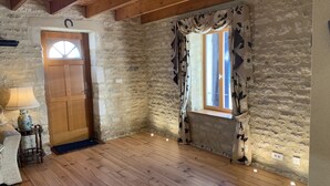 A rustic room with a wooden door, a window with floral curtains, stone walls, and a wooden floor. - La Grange – Spacious 3-Bedroom 19th-Century Barn with Private Garden (Le Coudreau Saint-Sigismond)