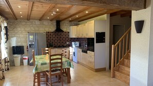 A cozy kitchen with wooden cabinets, a dining table with chairs, a washing machine, and a staircase. - La Grange – Spacious 3-Bedroom 19th-Century Barn with Private Garden (Le Coudreau Saint-Sigismond)