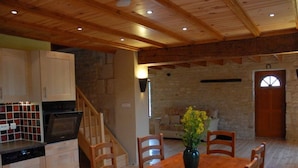 A spacious kitchen with wooden cabinets, a dining table, and chairs. There is a staircase leading to another level. - La Grange – Spacious 3-Bedroom 19th-Century Barn with Private Garden (Le Coudreau Saint-Sigismond)