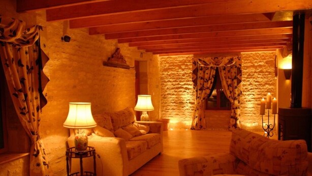 A cozy living room with wooden beams, stone walls, and a fireplace. There are two sofas, a coffee table, and lamps. - La Grange – Spacious 3-Bedroom 19th-Century Barn with Private Garden (Le Coudreau Saint-Sigismond)