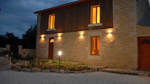 A two-story stone house with wooden siding, multiple windows, and a gravel driveway. - La Grange – Spacious 3-Bedroom 19th-Century Barn with Private Garden (Le Coudreau Saint-Sigismond)