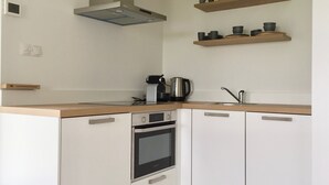 A modern kitchen with white cabinets, a built-in oven, a coffee maker, and two shelves with kitchenware. - B&B depolderschuur is an independent home (Tienhoven)