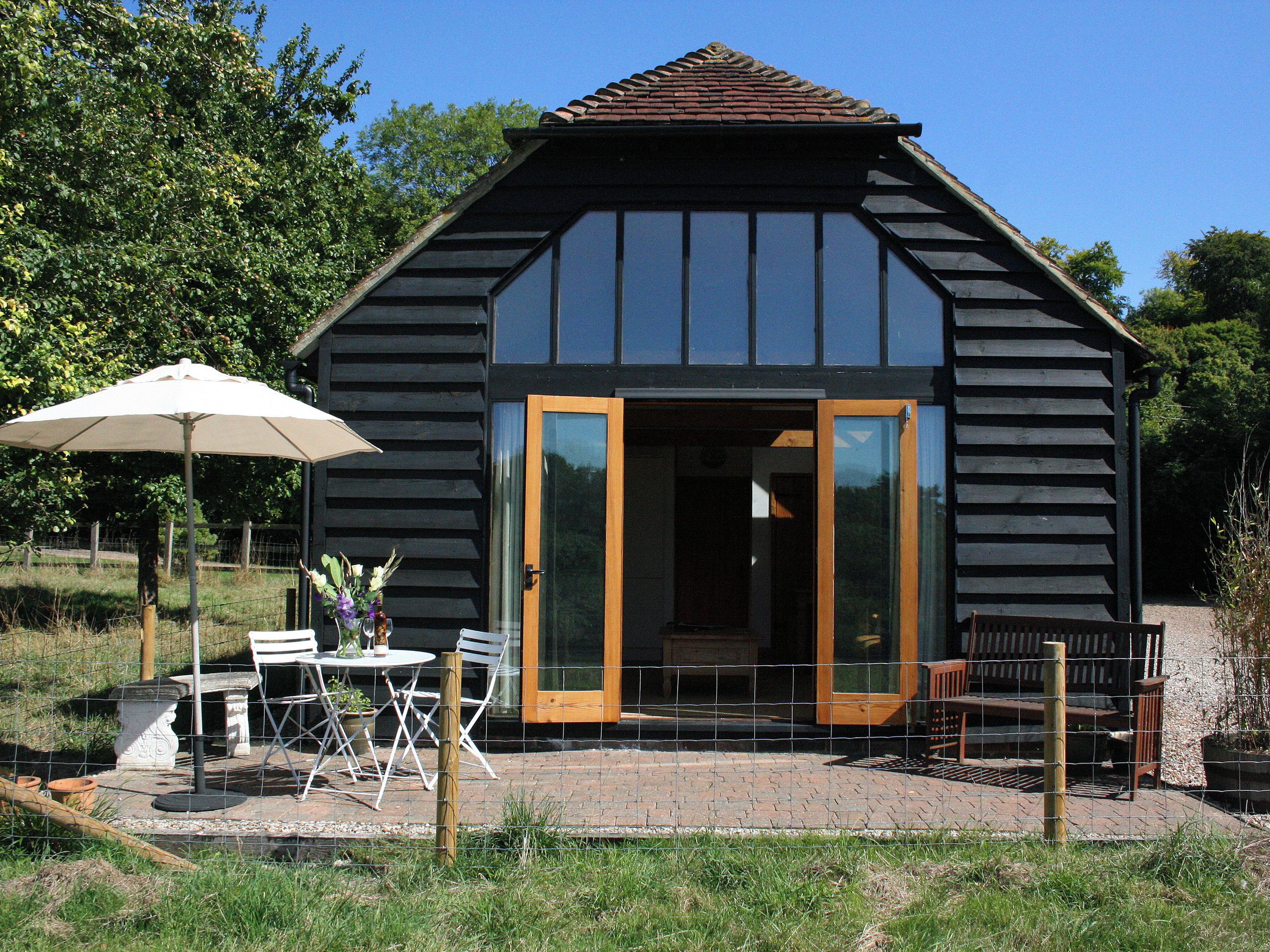 A wooden cabin with a large sliding glass door, outdoor seating, and a table with chairs.
