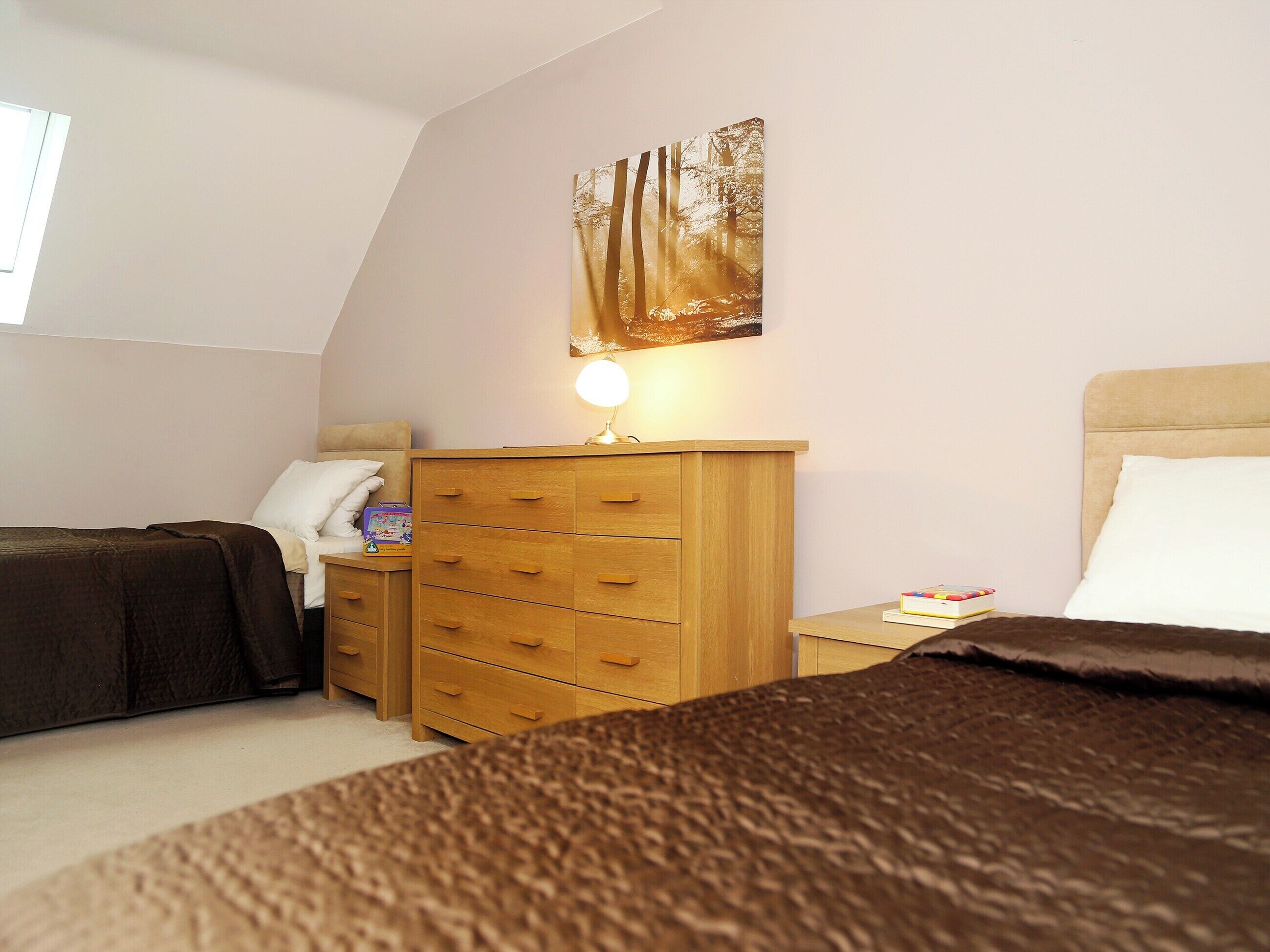 Ein Schlafzimmer mit zwei Betten, einem Holzschrank, einem Nachttisch mit Lampe und einem Bild an der Wand.
