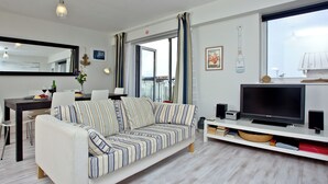 A modern living room with a sofa, TV, and a dining area with a table and chairs. - Apartment 7, Ocean 1 (Newquay)