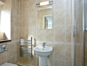 Casa de banho com lavatório, espelho, porta-toalhas e chuveiro.