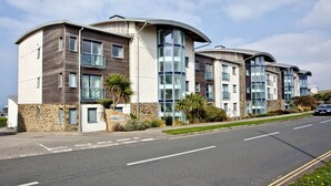 A modern multi-story building with a curved facade, large windows, and a stone base. - Apartment 7, Ocean 1 (Newquay)