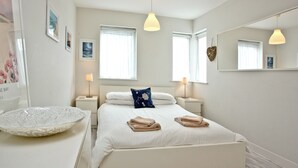 A bedroom with a bed, bedside tables, a mirror, and a window. - Apartment 7, Ocean 1 (Newquay)