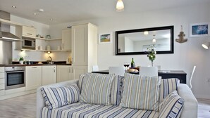 A modern living room with a sofa, a dining table, and a kitchen area with cabinets and appliances. - Apartment 7, Ocean 1 (Newquay)