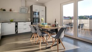 Una cocina moderna con armarios blancos, horno empotrado y comedor con mesa y sillas.