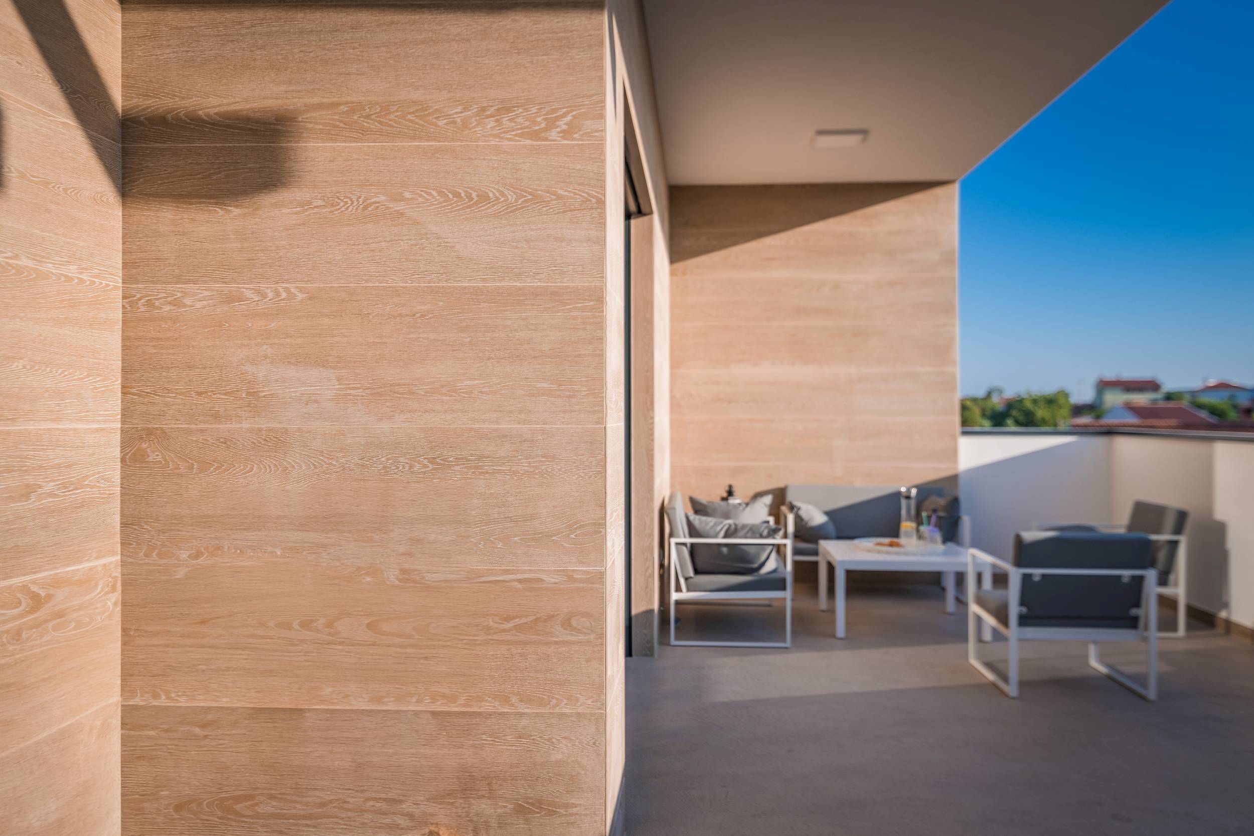 A modern balcony with a wooden floor, a white table, and two chairs.