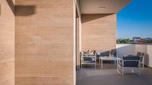 Un balcón moderno con suelo de madera, una mesa blanca y dos sillas.