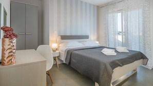 Una habitación de hotel moderna con cama, mesita de noche, lámpara y un escritorio con silla.