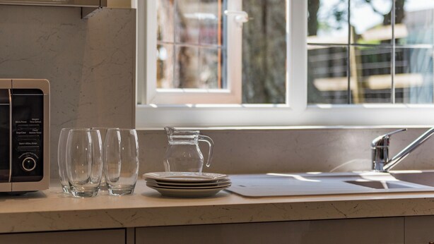 A kitchen with a microwave, glassware, plates, and a pitcher on the counter. - Charming barn conversion with enclosed private garden. (Sedlescombe)