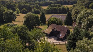 A rural house with a sloped roof, surrounded by dense trees and open fields. - Charming barn conversion with enclosed private garden. (Sedlescombe)