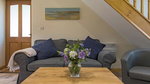 A living room with a grey sofa, a wooden coffee table, and a painting on the wall. - Charming barn conversion with enclosed private garden. (Sedlescombe)