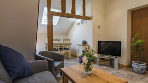 A cozy living room with a wooden coffee table, a grey sofa, and a TV on a stand. - Charming barn conversion with enclosed private garden. (Sedlescombe)