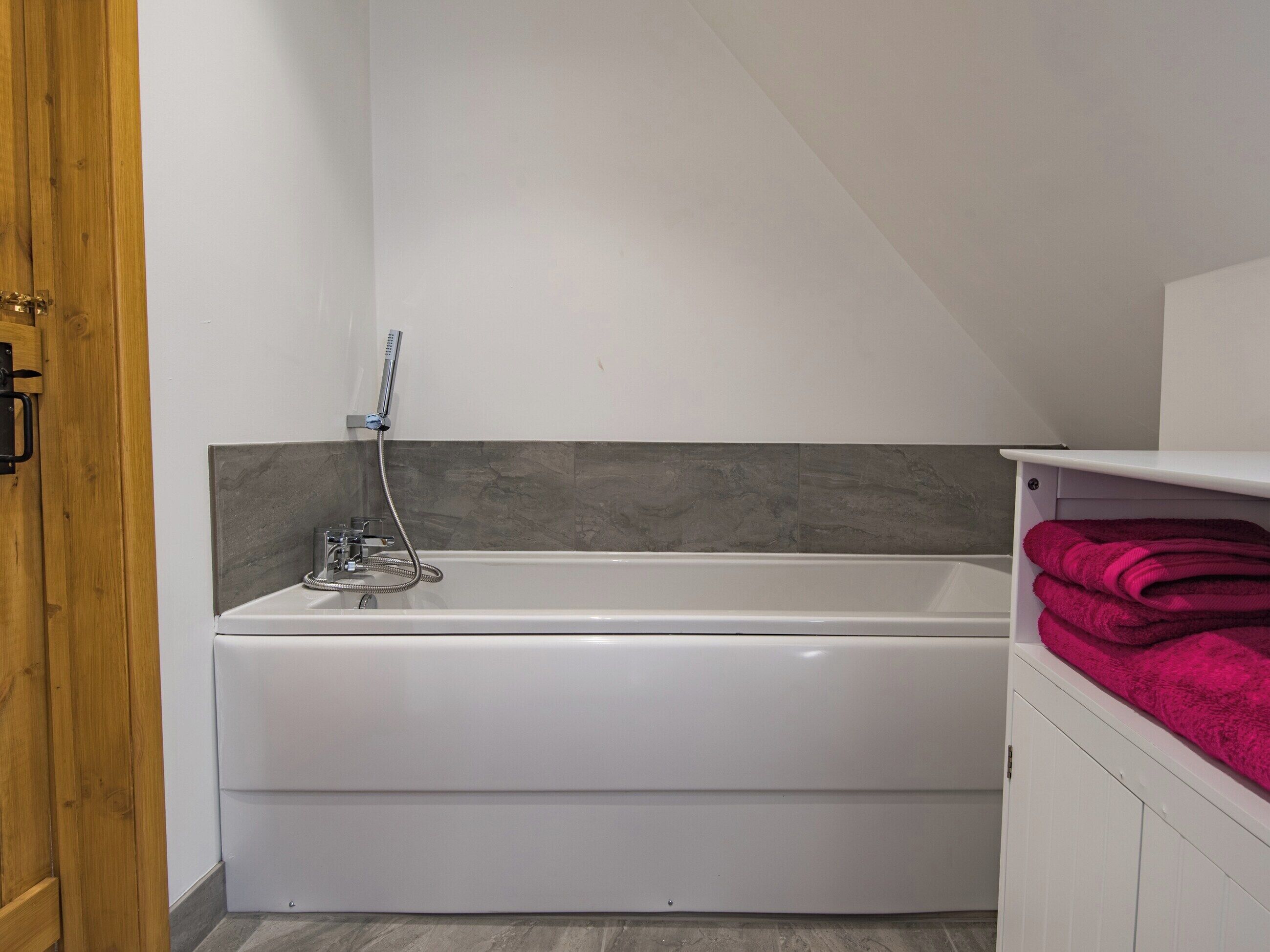 A modern bathroom with a white bathtub, a showerhead, and a wooden door.